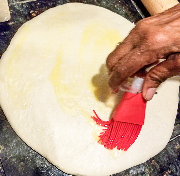 Rolled out bread dough and melted butter being brushed on the dough.