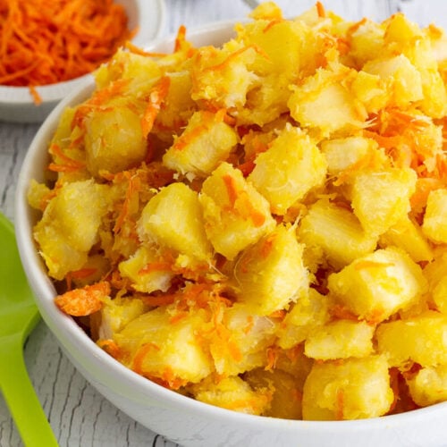 Cassava with butter and carrots in a white bowl.