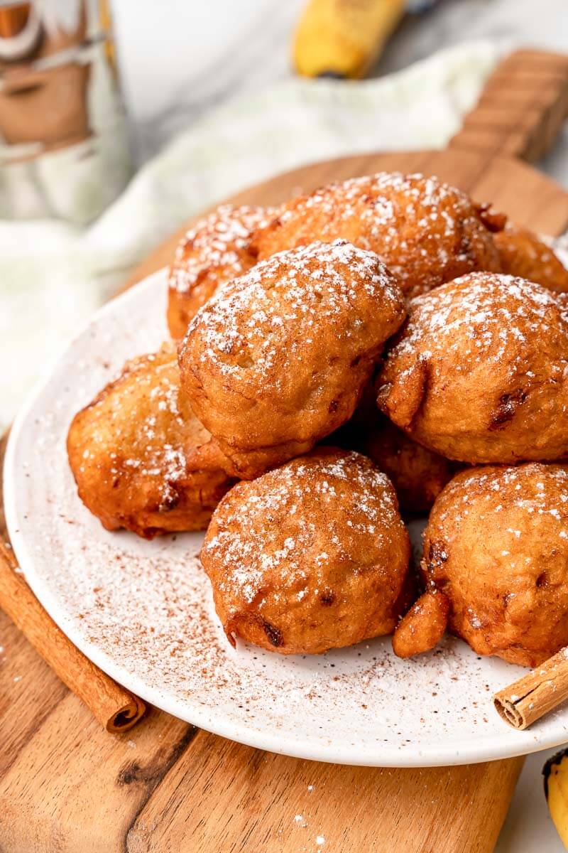 Finished fried banana fritters on a white plate dusted with cinnamon.