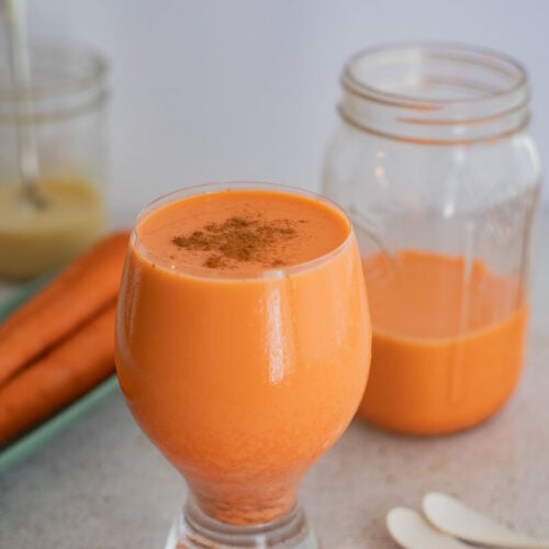 A picture of a full glass of carrot juice topped with some cinnamon.