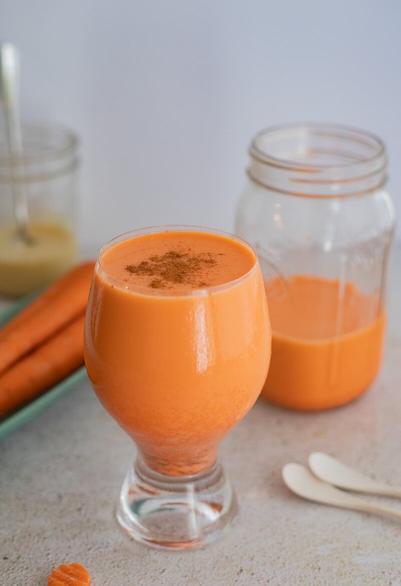 A picture of a full glass of carrot juice topped with some cinnamon.
