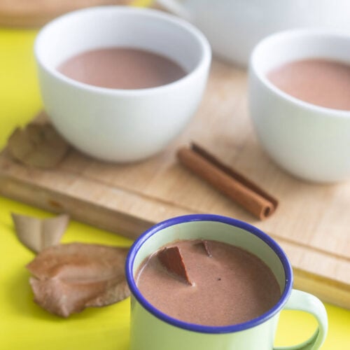 Enamel Cup of Caribbean Cocoa Tea with Two White Mugs in the Background.