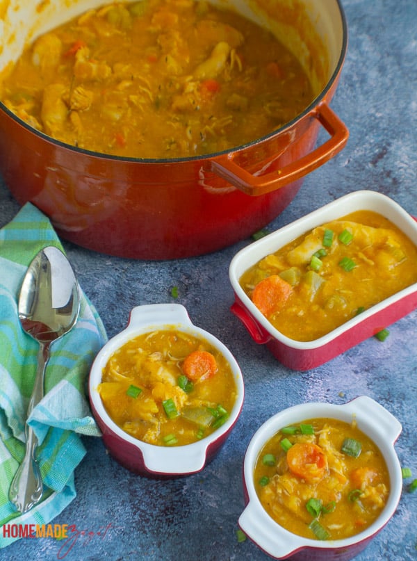 A large dish of Caribbean chicken soup, with smaller serving of soups in red bowls