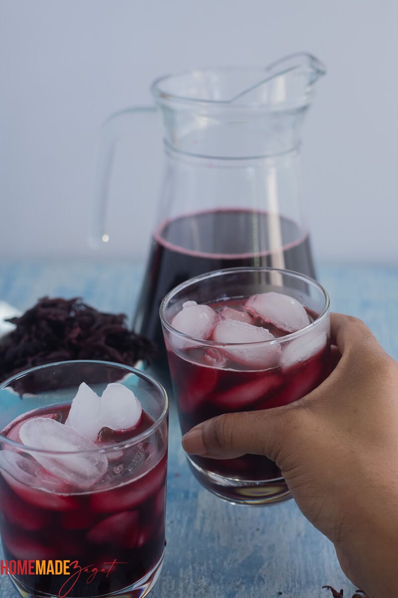 Two glasses of Caribbean sorrel drink with ice and boiled sorrel leaves