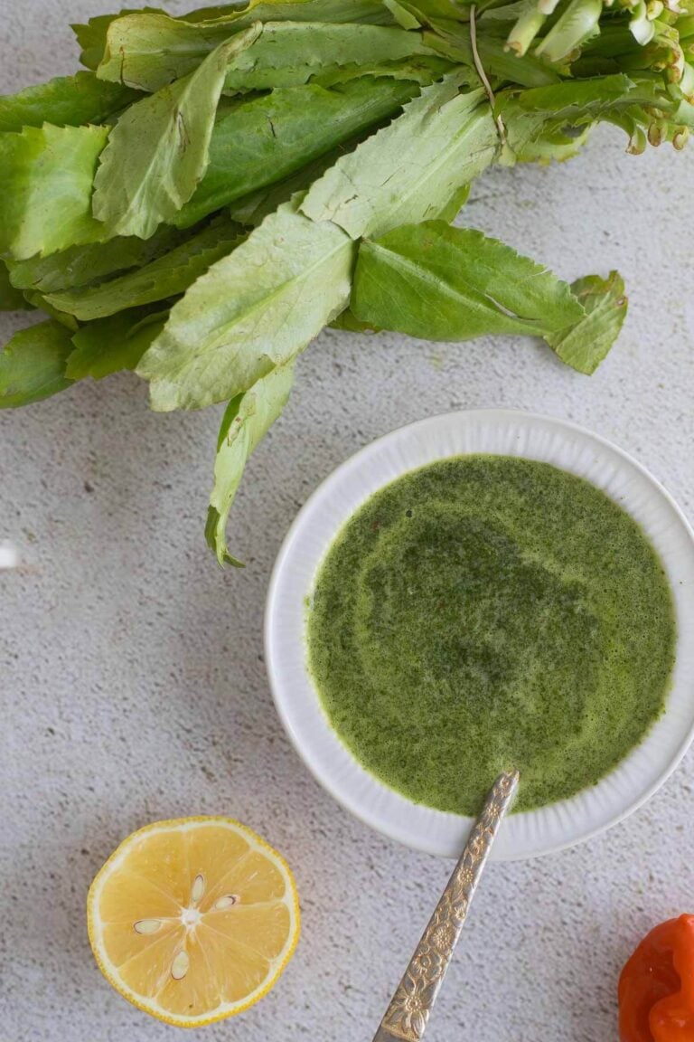 Mixed chadon beni sauce with a bunch of fresh chadon beni leaves on top of a board with a slice of lemon.