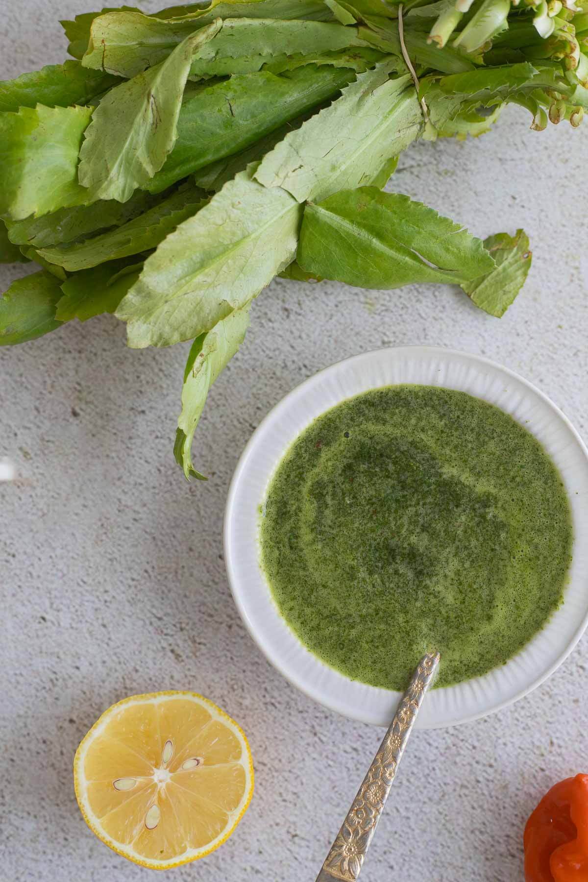 Mixed chadon beni sauce with a bunch of fresh chadon beni leaves on top of a board with a slice of lemon.