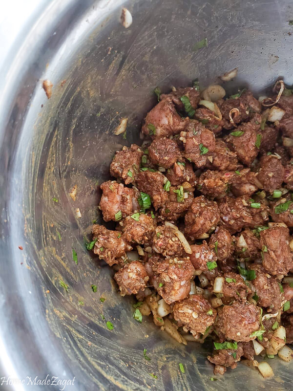 Chicken neck pieces seasoned up with geera and curry with fresh herbs and spices in a silver bowl.