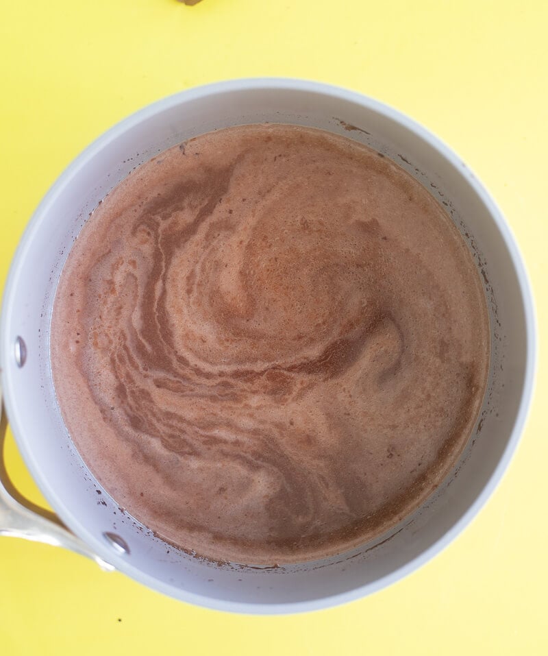 Overhead view of milk added to simmered chocolate with water and spices.
