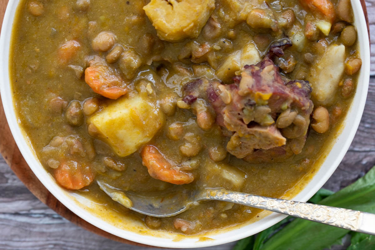 A bowl of pigeon peas soup with smoked bone and various ground provisions.