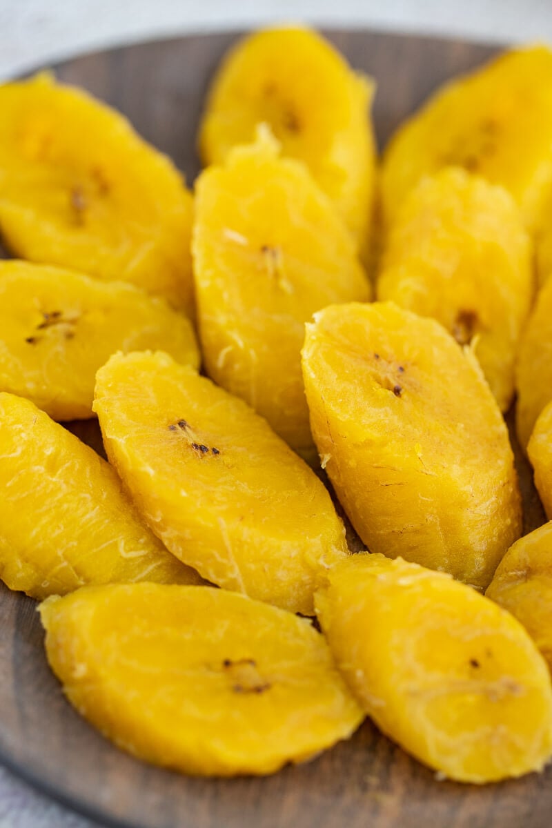 Close up of yellow plantains, boiled and sliced on a plate.