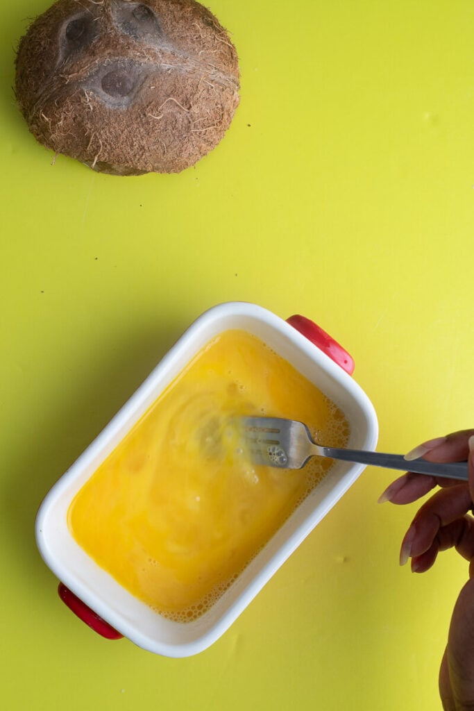 Slightly beaten eggs in a red bowl on a yellow backdrop.