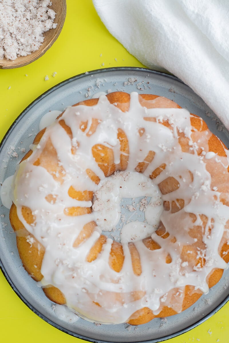 Cake covered in coconut glaze with shredded coconut on a blue plate.