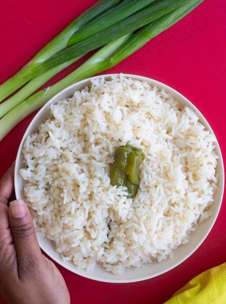 Coconut rice in a white bowl, with scallion and a yellow napkin on a red counter top.
