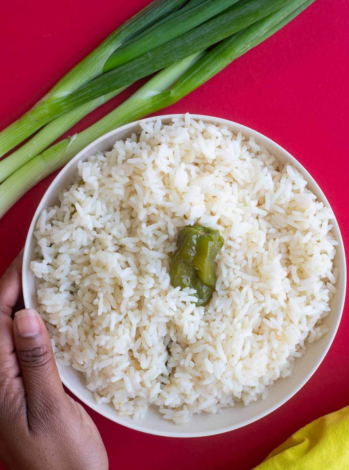 Coconut rice in a white bowl, with scallion and a yellow napkin on a red counter top.