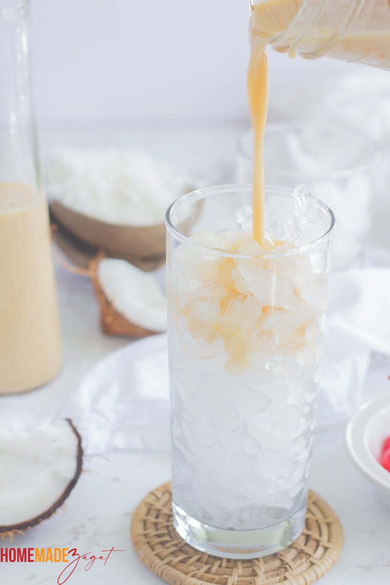 Pouring punch into a tall glass of ice with some leftover in the background