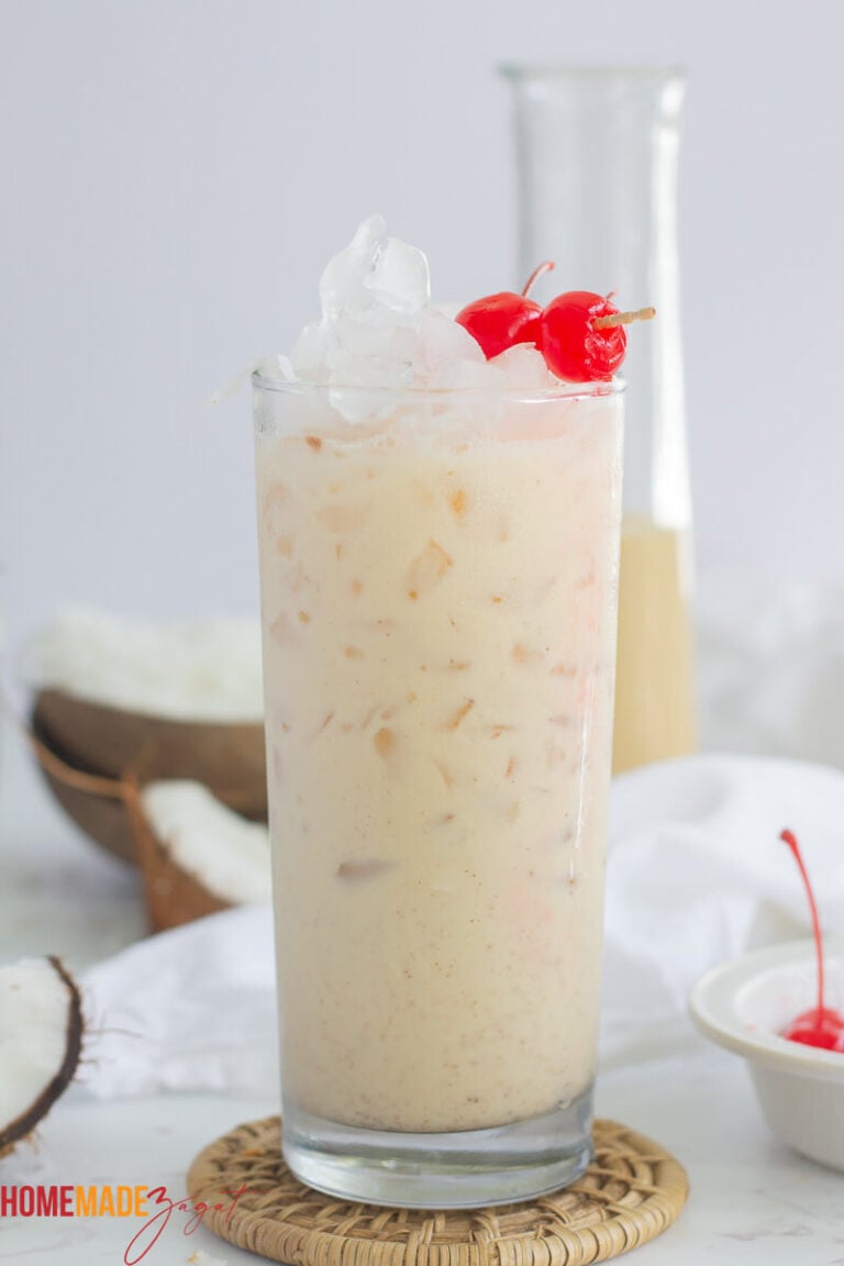 Coconut Ponche de creme in a tall glass with ice and red cherries