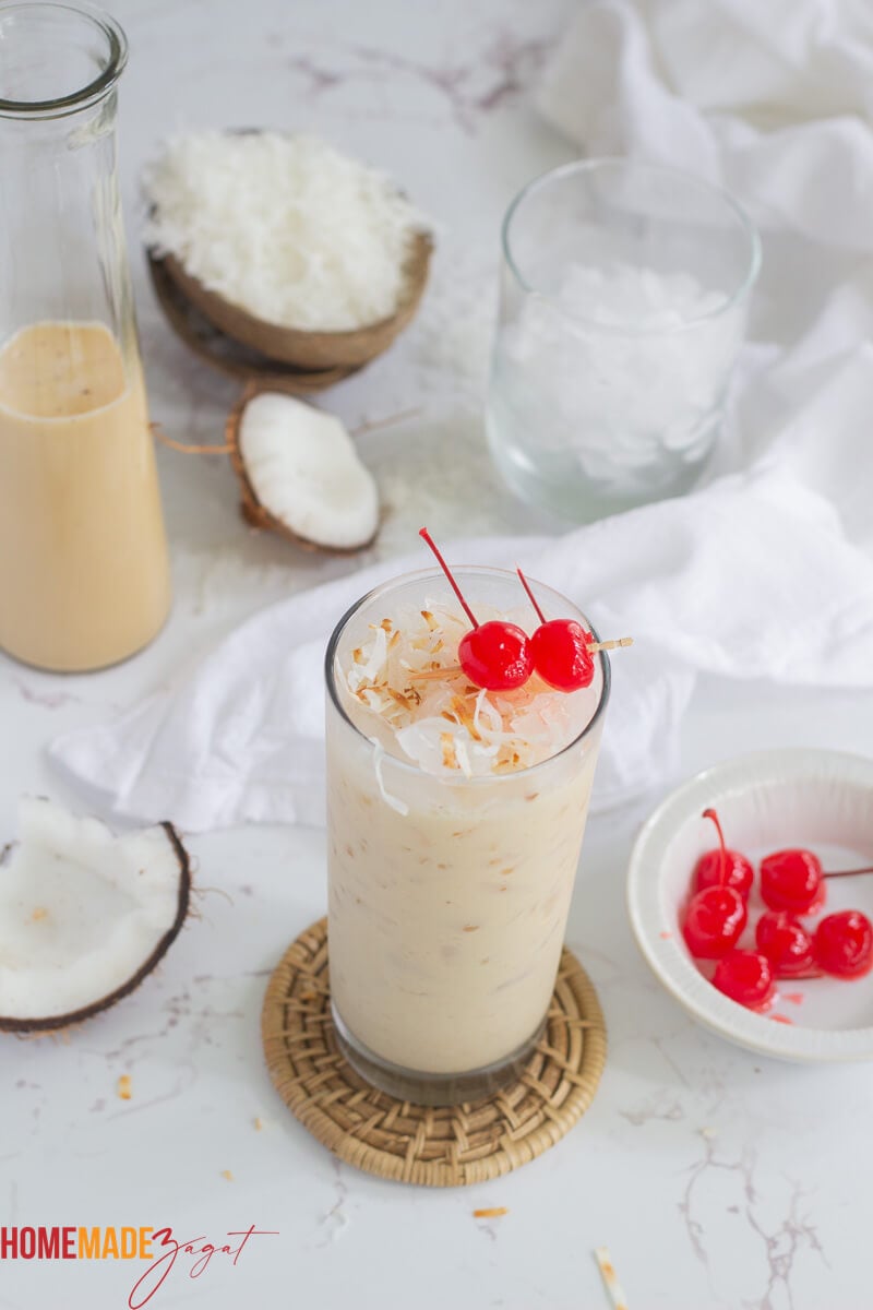A full tall glass of coconut ponche de creme, with coconut shavings in the background