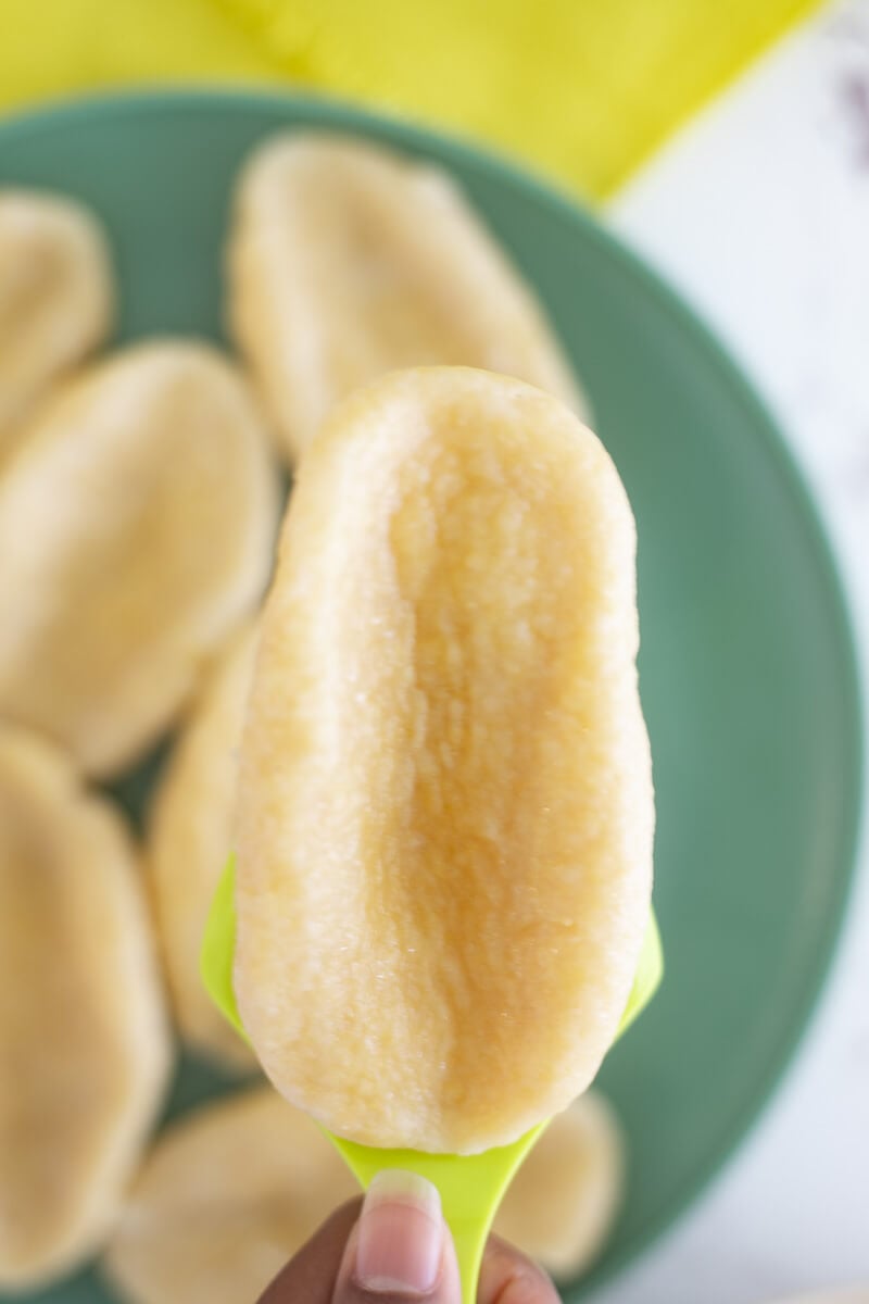 Boiled cornmeal dumpling completed and ready to eat, being held up with a green spatula.