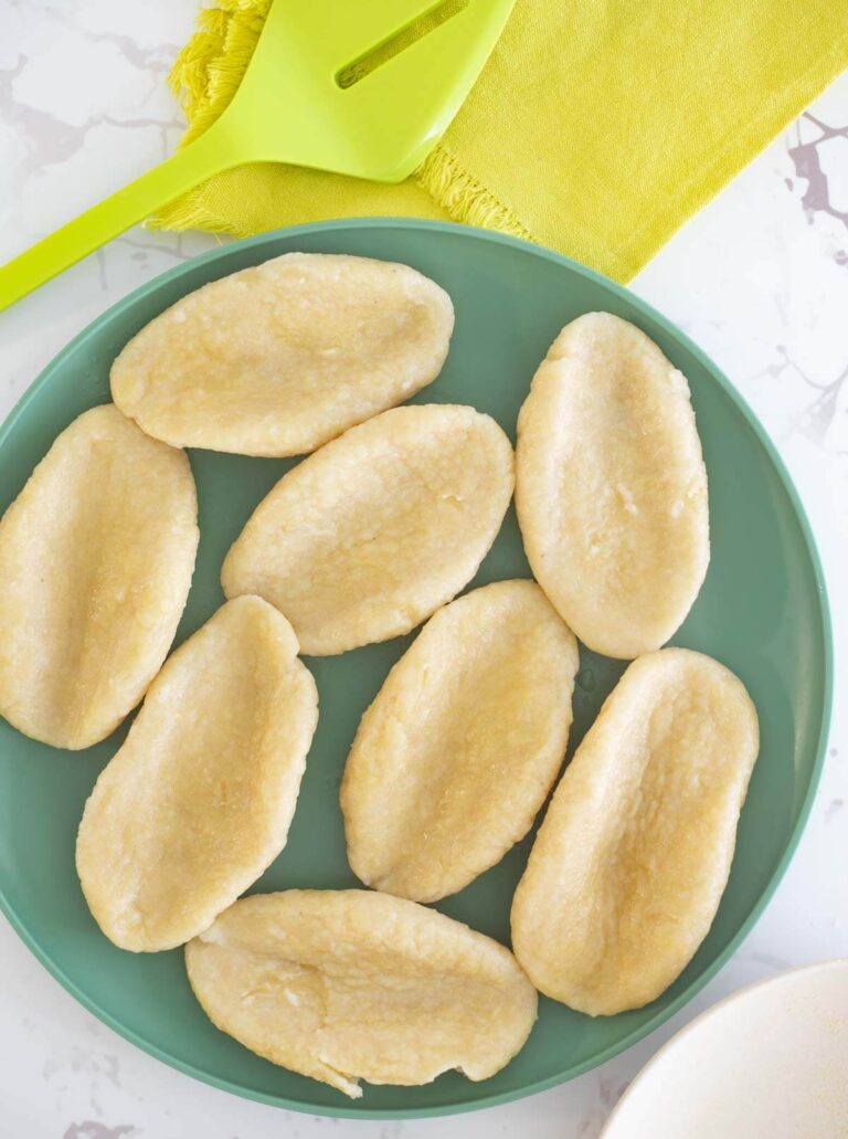 Boiled cornmeal dumplings on a green plate with a white background and a green spatula on a green napkin.