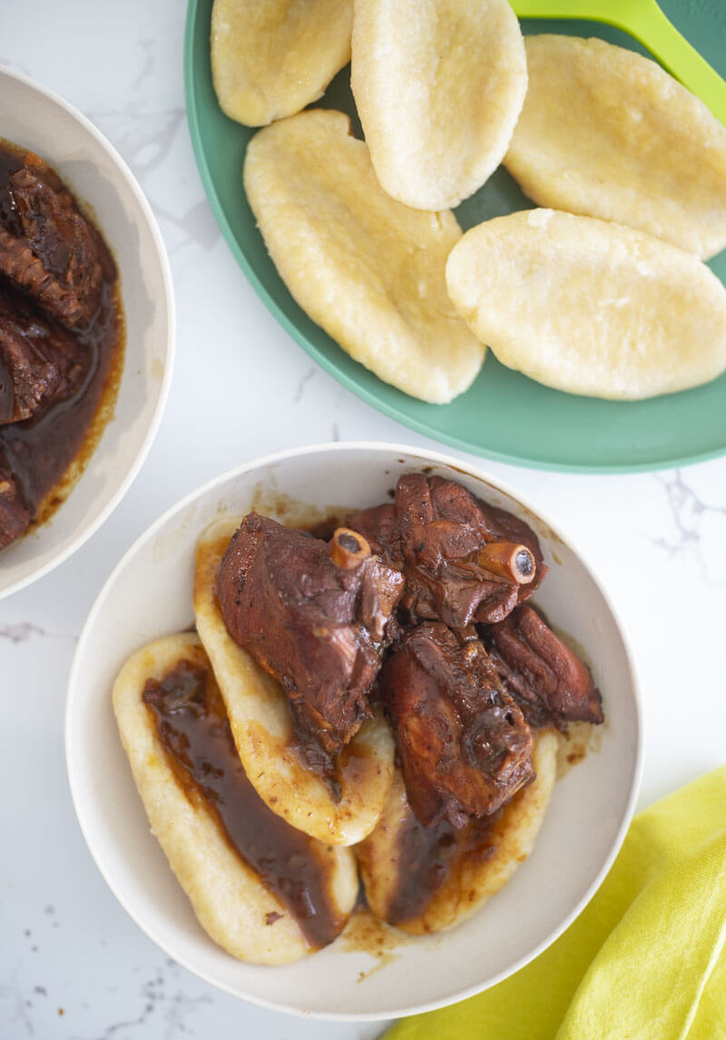 Jamaican cornmeal dumplings on a white plate served with some stewed chicken.