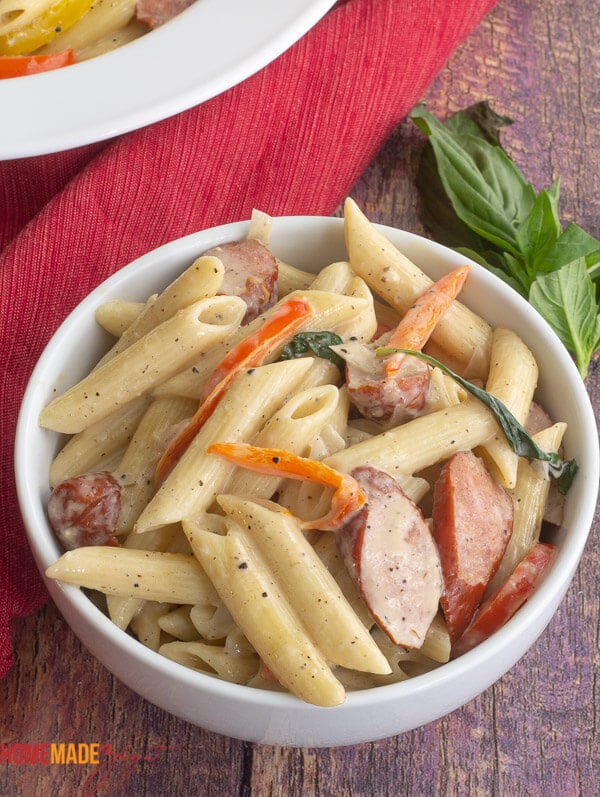 A big white bowl of creamy pasta with sausage and bell peppers.