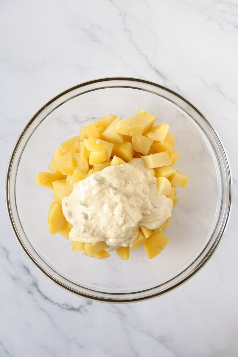 A bowl of cubed potatoes with mayonnaise mixture.