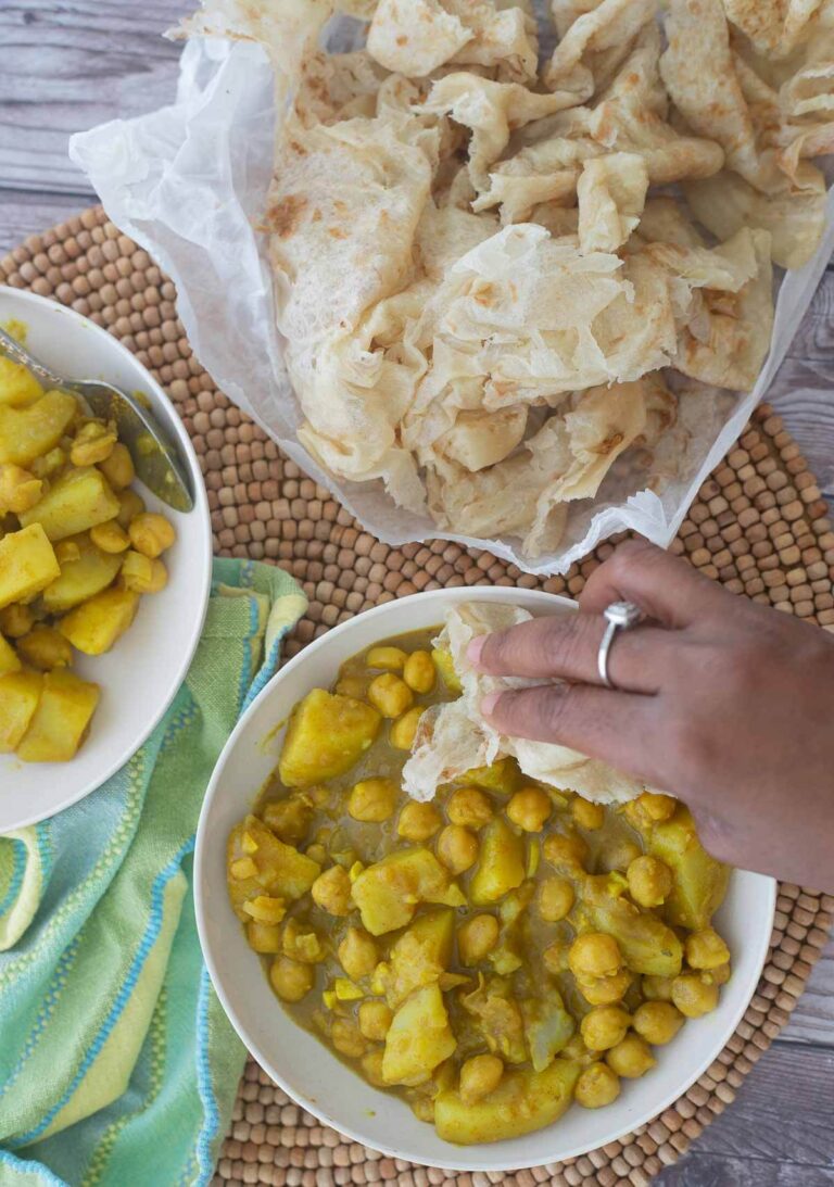 Two serving bowls of channa aloo curry with a serving of partha roti.