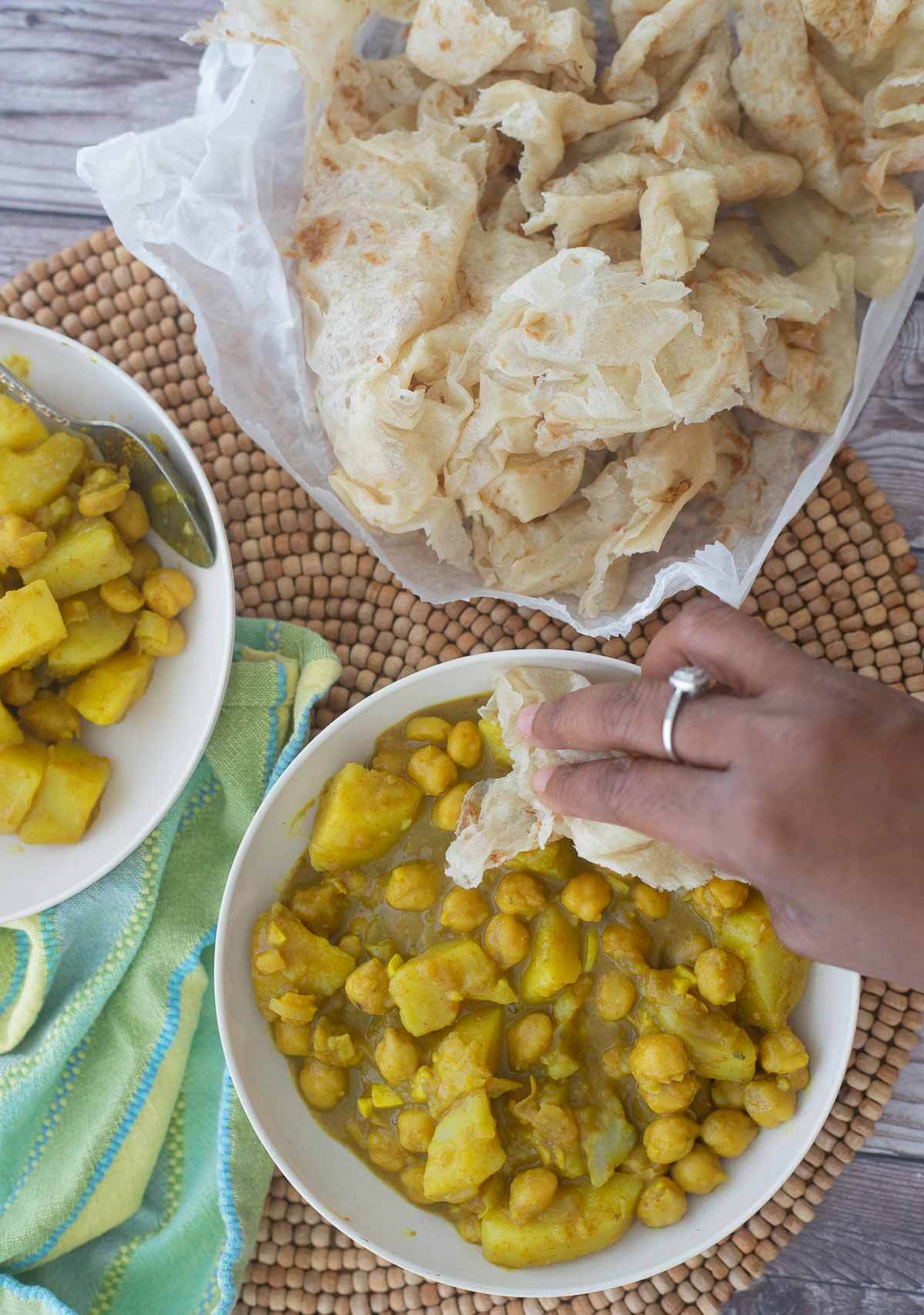 Two serving bowls of channa aloo curry with a serving of partha roti.