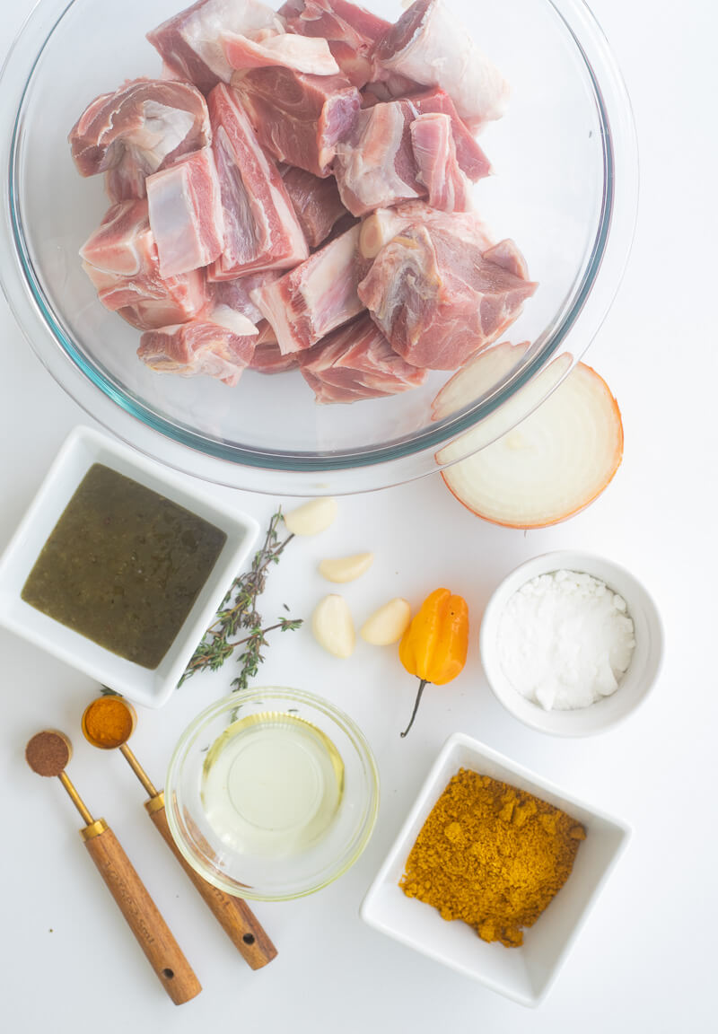 Ingredients for cooking curry goat portioned out in bowls on a white countertop..