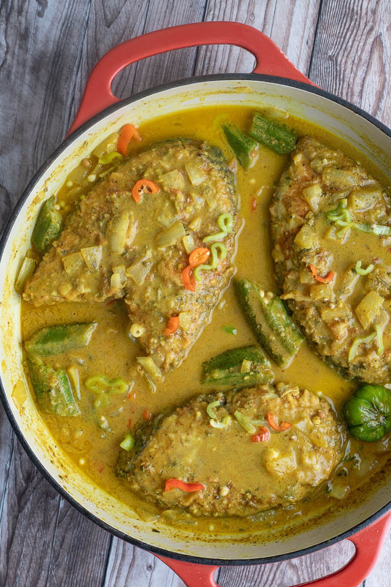 A sauce pan of three pieces of king fish in a curry coconut milk sauce.