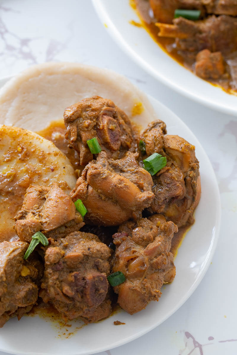 Delicious curry stew chicken served with Caribbean boiled dumplings on a white plate.