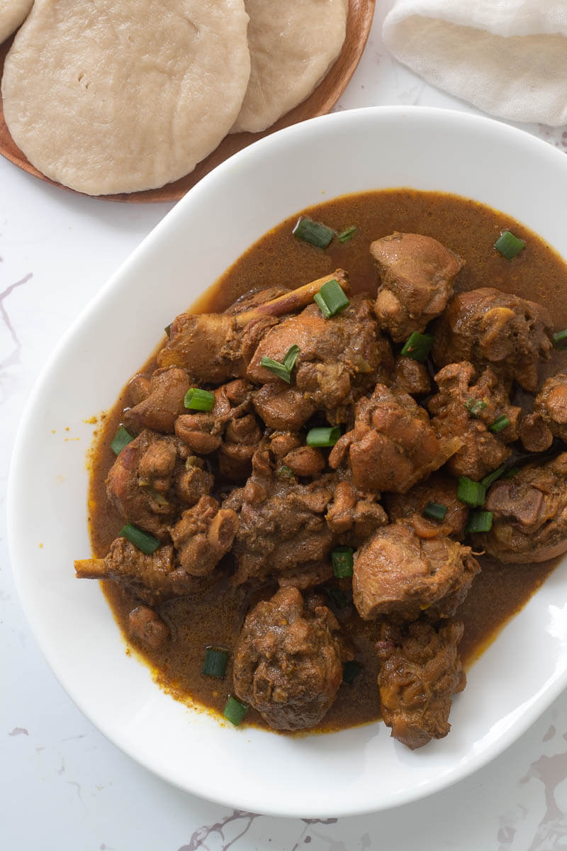 Curry stew chicken Trinidad style on a white serving plate and garnished with scallions.