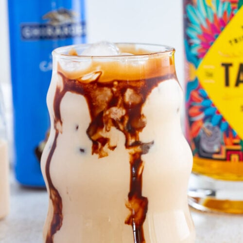 Creamy jamaican rum creme with chocolate garnish running down the sides of a glass on a creme counter top with a bottle of Caramel syrup in the back.
