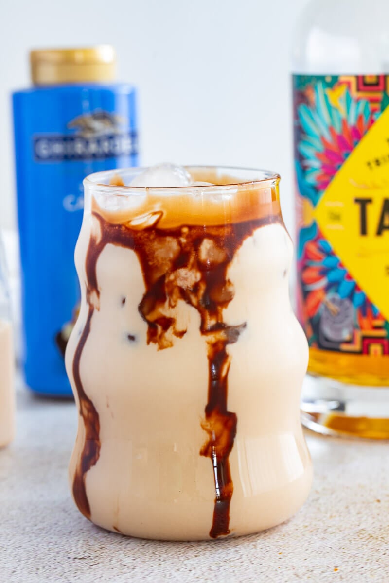 Creamy jamaican rum creme with chocolate garnish running down the sides of a glass on a creme counter top with a bottle of Caramel syrup in the back.