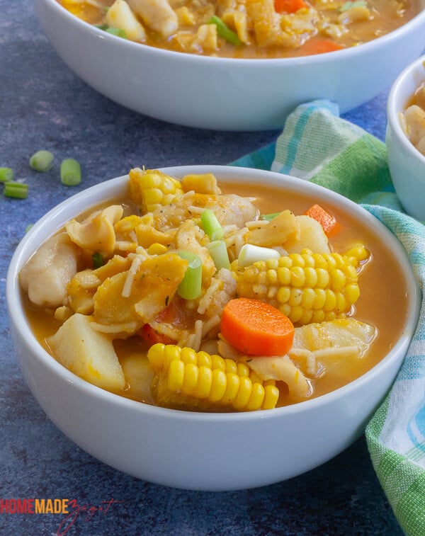 Close up of a full white bowl of conch soup with corn, potatoes, carrots and dumplings