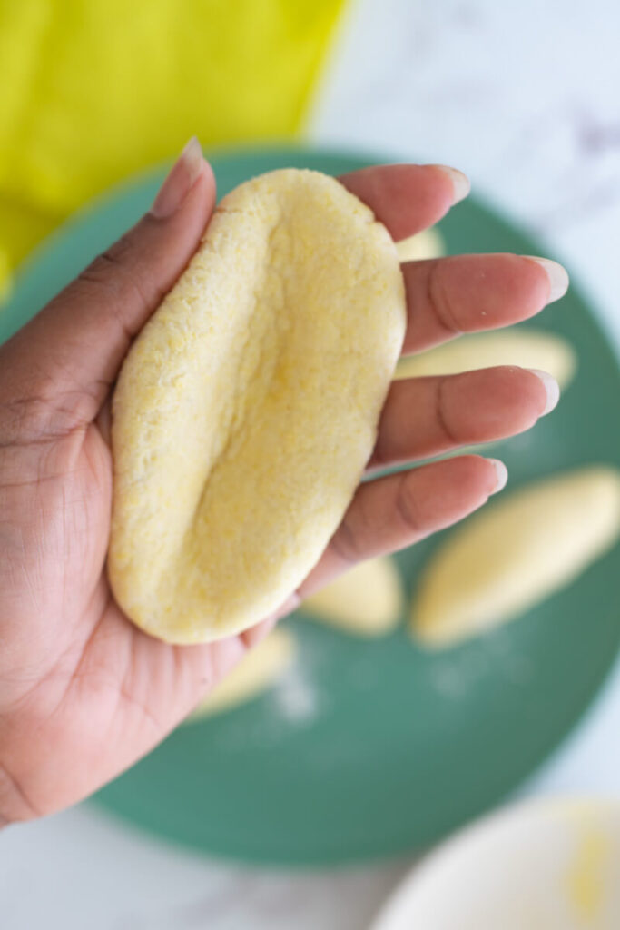 A hand holding one Jamaican cornmeal dumplings made with an indent to make a concave shape.