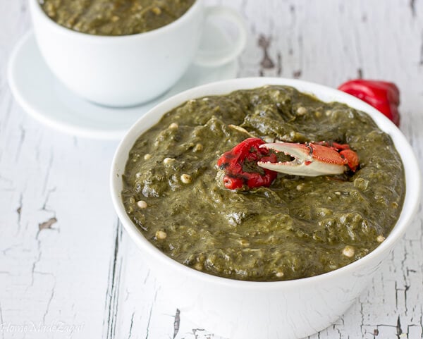 A bowl of callaloo with crab on a white counter top with a smaller bowl in the backc with callaloo.