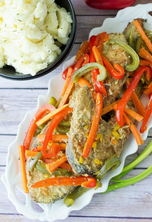 Slices of fish with veggies on top in a white plate and a bowl of mashed potatoes