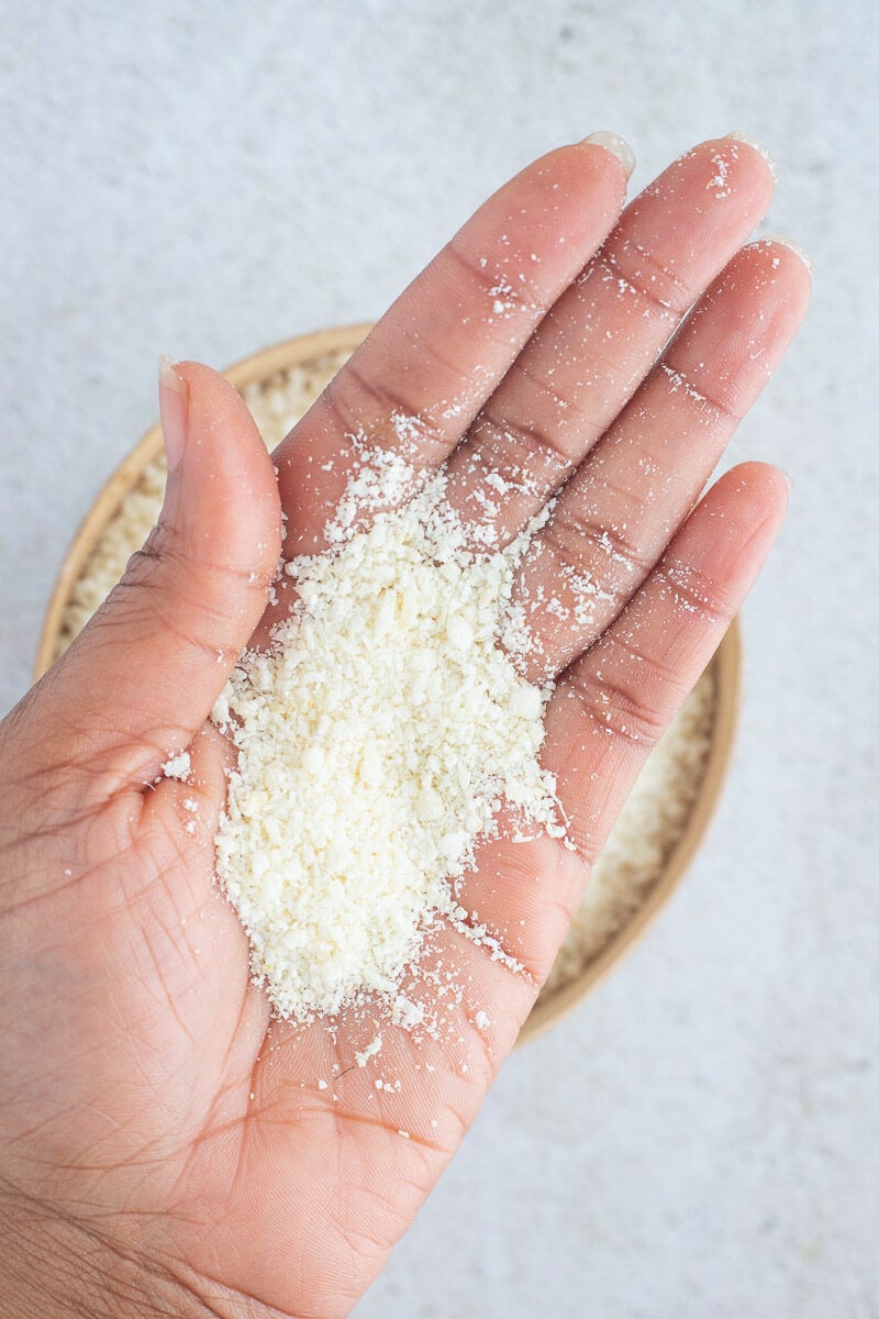 A close up of the coarse grains of farine in a hand over a calabash of farine.