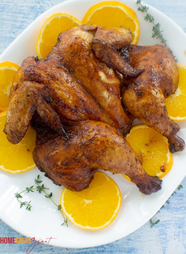 Finished roasted spatchcocked chicken on a white plate with orange slices.