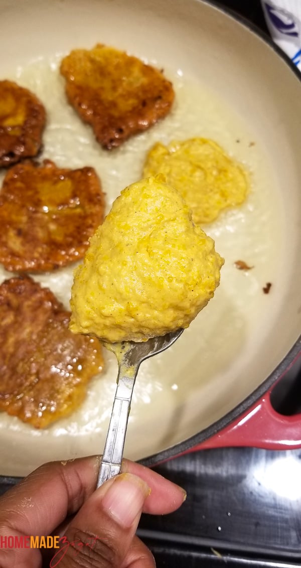 Spoonfull of fritter batter with other fritters frying in the background