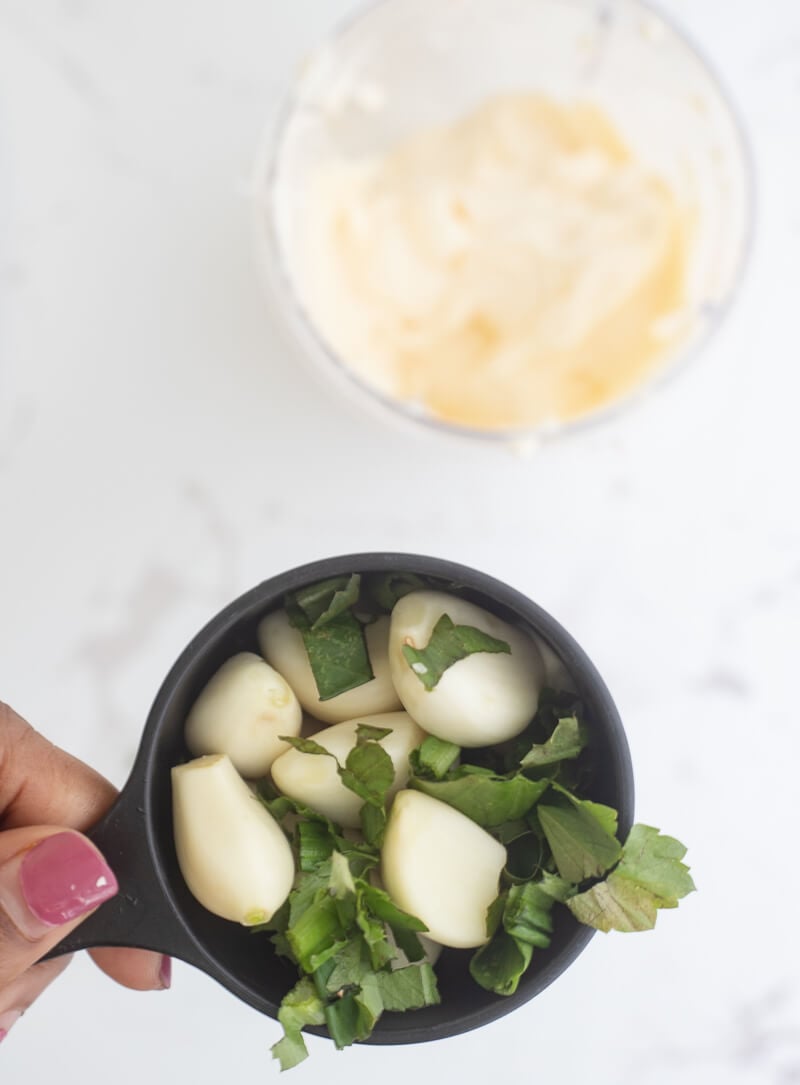 A measuring cup of cleaned garlic cloves and chopped up chadon beni leaves to get ready to blend to make trini garlic sauce.