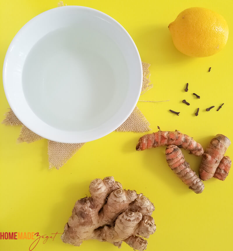 A white bowl with water, some ginger, tumeric, clove and lemon. Ingredients to make the tea