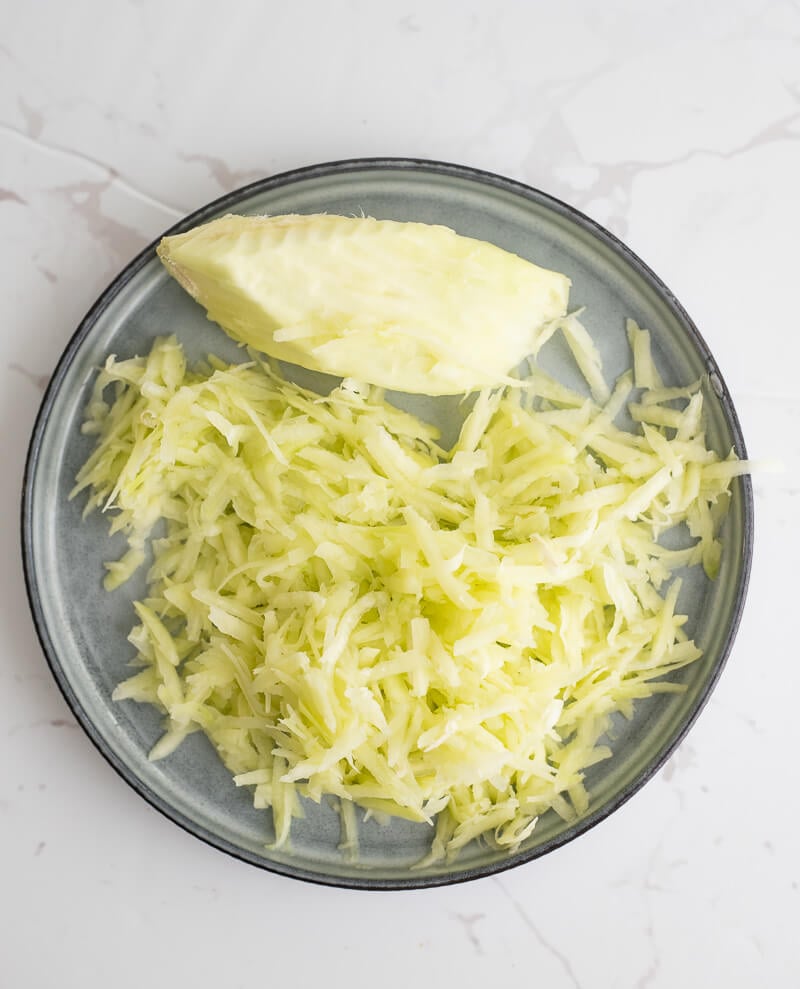 Grated mango on a blue plate with a green mango seed.