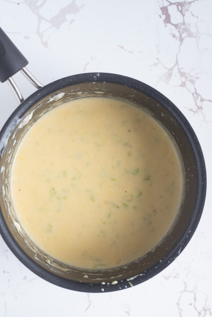 The creamy white cheese roux needed to for making the pie in a black sauce pan.