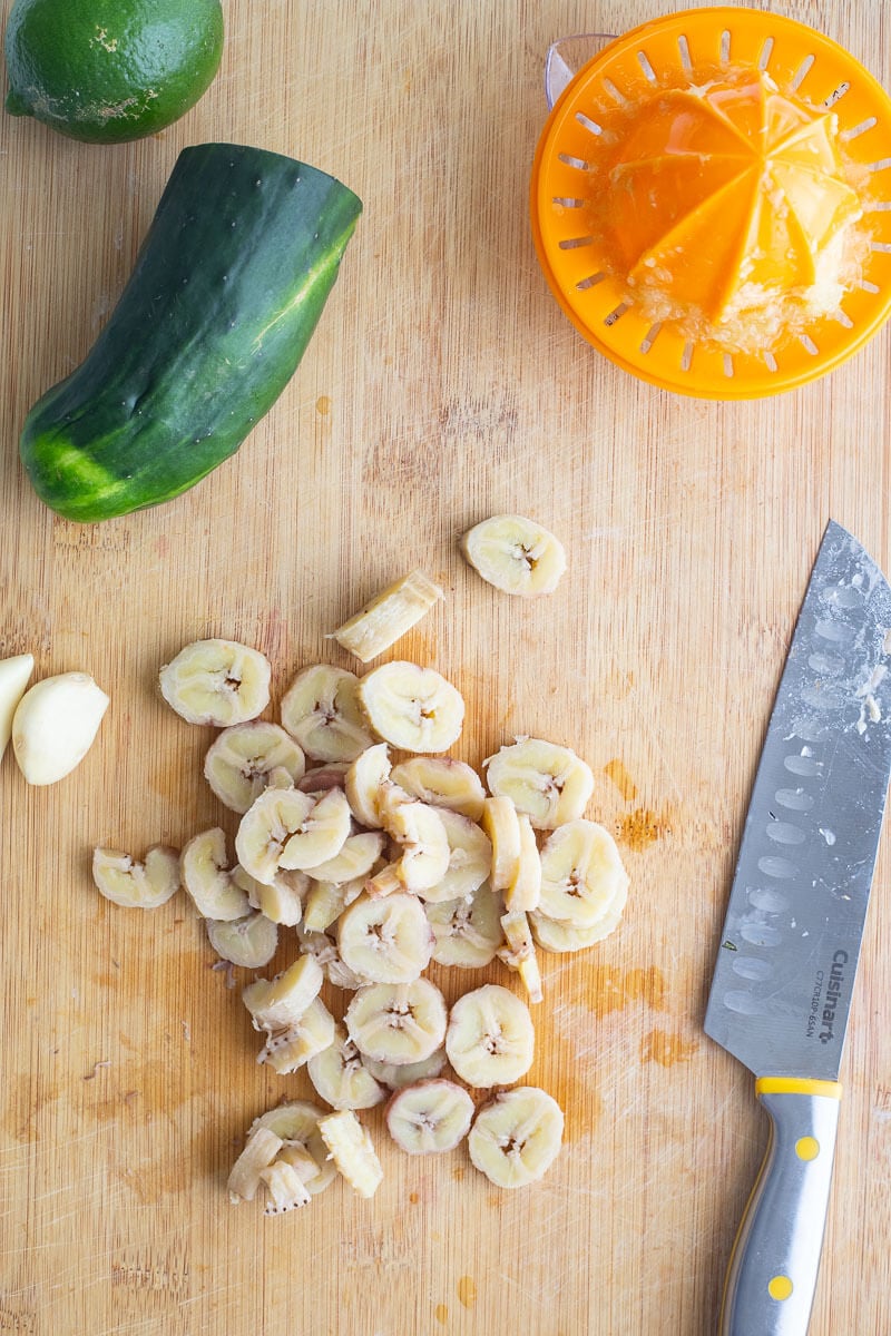Boiled green fig cut into 1" pieces on a brown cutting board with other herbs.