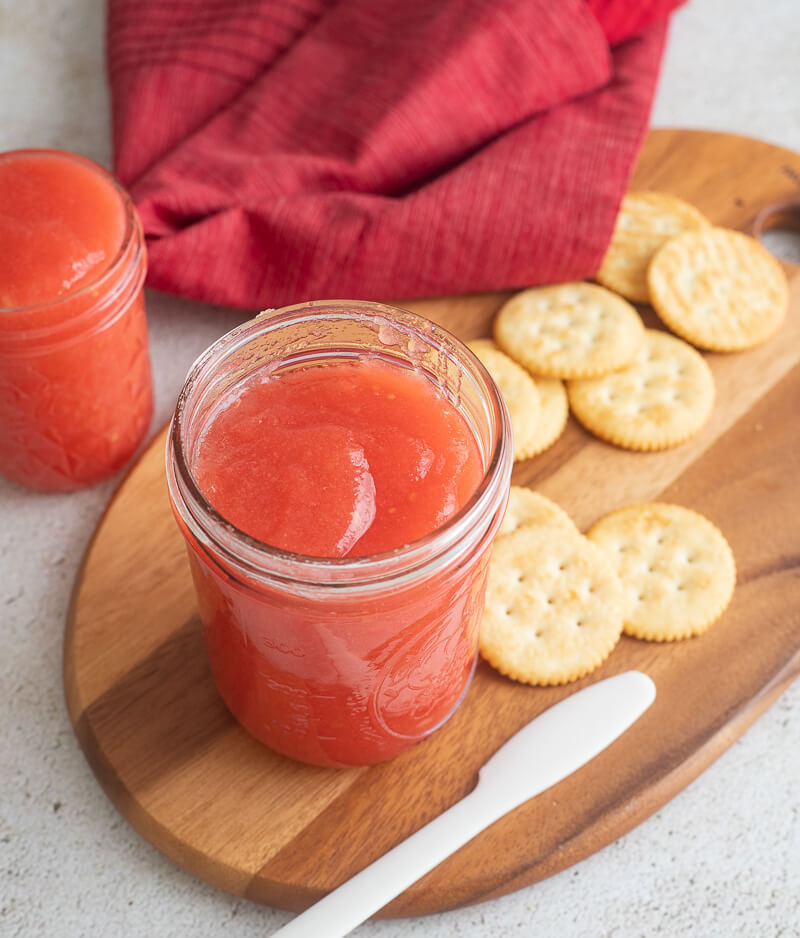 Completed guava jam in a jar on top a wooden cutting board with a white knife.