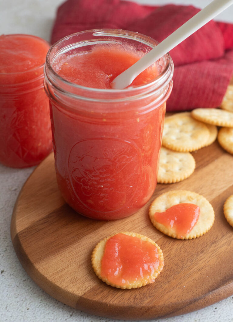 Two canning jars of guava jam on top of a wooden bread board.