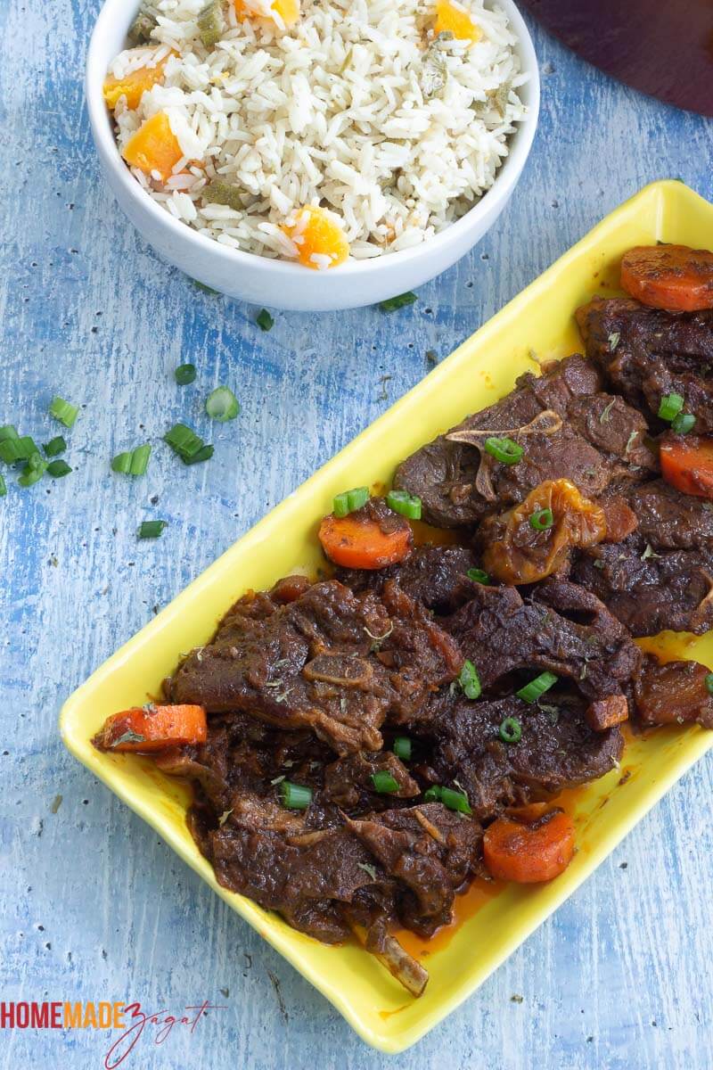 Lamb stew on layed out in a yellow plate with a white bowl filled with okra and rice