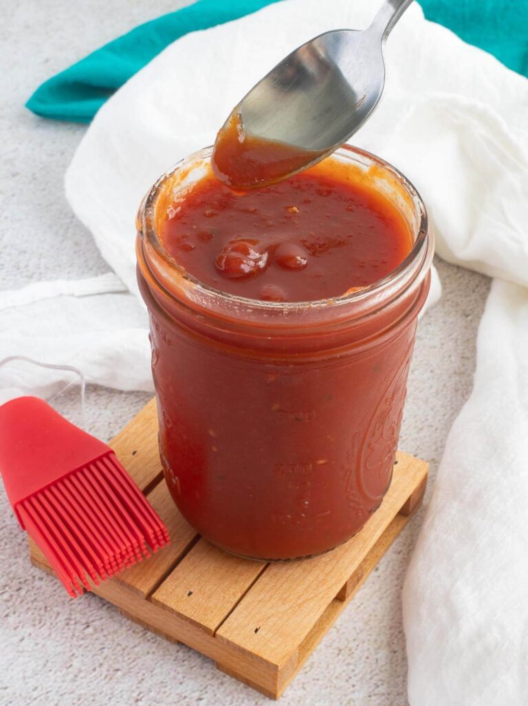 A bottle of Caribbean bbq sauce in a mason jar without the cover and a spoon hovering over the top.